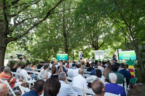 Pubblico seduto in un parco, ascolta un evento con pannelli verdi sullo sfondo